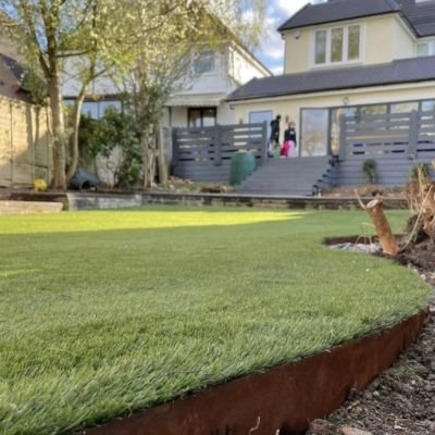 A newly installed, pristine green sod lawn featuring a curved metal garden edge in a residential backyard, leading up to a modern grey composite deck.